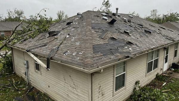 Storm roof damage | two rivers roofing, inc a home with severe storm roof damage showing torn shingles, exposed underlayment, scattered debris, and fallen branches across the roof, highlighting the need for storm damage roof repair.
