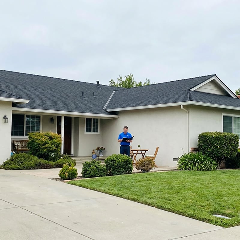 a well-maintained sacramento home with a visible roof and a professional reviewing notes outside, illustrating how roof maintenance plans support long-term roof care and prevention.